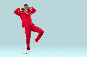 Fototapeta na wymiar Happy cheerful joyful excited confident attractive good looking young African American man wearing cool modern red suit dancing on light blue blank copyspace background. Fashion, party, fun concept