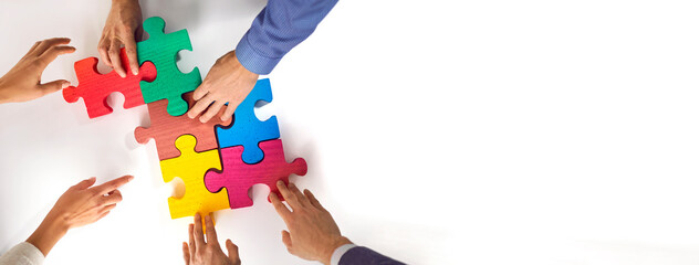 Business team matching jigsaw puzzle parts. Young people connect colorful red, green, pink, blue, yellow jigsaw pieces on white office table. Crop shot. Teamwork concept. Copy space banner background - Powered by Adobe