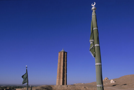 Green flags decorating a saint or holy man's tomb flutter below a towering brick minaret on the road into Ghazni, Afghanistan.