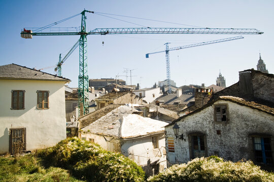 Giant construction cranes loom over the old slate rooftops of Lugo, Galicia, Spain.