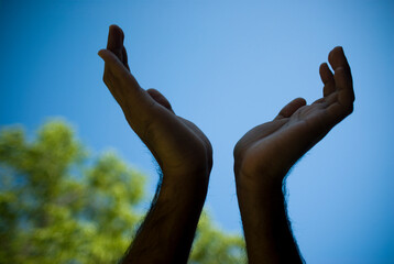 Two open hands reach out into the sky.