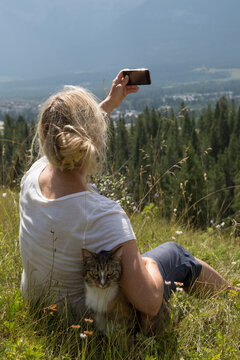 Woman takes photo with cat in mountain meadow