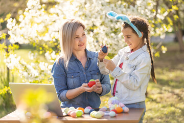 mother and daughter paint easter eggs with laptop, record lessons on a webcam with a laptop. mother and daughter are preparing for the holiday together.