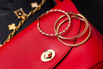 Gold ring earrings and costume jewelry lie on a red leather bag