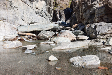 Pond with crystal clear water and small pebbles and sands formed by Lillaz waterfall (Cascate di Lillaz) in granite crack, close view, Aosta valley, Italy