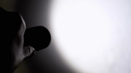 Person Shines a Flickering Flashlight on Wall in a Dark Room. Silhouette of a hand with a flashlight. Abstract shimmering, flashing, pulsing glare beam of light. Spot. Strobe effect. Shadow. Police.