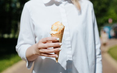 Close-up of woman's hand holding an ice cream waffle cone on sunny day outdoors, front view