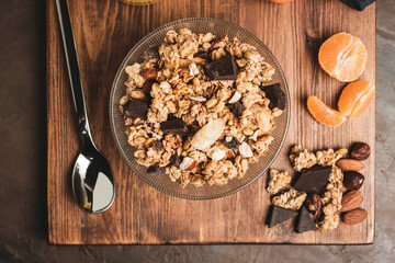 Granola cereal oatmeal with chocolate, fruist and nuts in a bowl on dark wooden board, top view