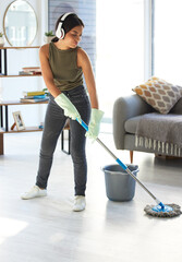 Fototapeta premium Music, cleaning and mop with woman in living room streaming while housekeeping, sanitary and hygiene. Mobile radio, podcast and listening to headphones with girl cleaner mopping floor for hospitality