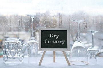 Fototapeta Dry January, month without alcohol. Chalk text, caption Dry January on blackboard, chalk board. Empty vine and beer drinking glasses. Window with raindrops, grey winter city skyline on background. obraz