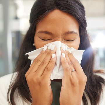 Woman, sneeze and tissue for flu, covid and safety in workplace with hands on face for health by blurred background. Corporate black woman, office and sick with toilet paper, nose and covid 19 virus