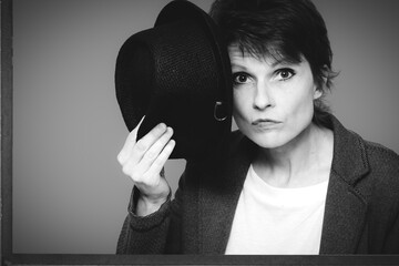 Schwarzweiß Studioaufnahme einer schönen Frau 50 plus mit Hut auf dunklem Hintergrund