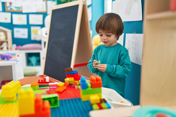 Adorable toddler playing with construction blocks standing at kindergarten