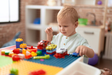 Adorable toddler playing with car and toy and construction blocks sitting on table at kindergarten