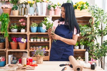 Middle age hispanic woman florist holding bouquet of flowers at florist