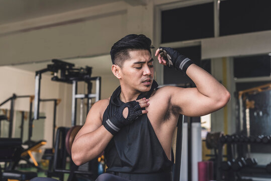 An asian man assessing his shoulder or chest muscle for any pain or stiffness. Trying to move his arm to confirm an injury.
