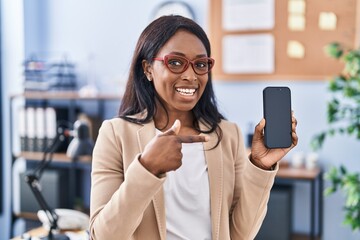 African young woman holding smartphone showing blank screen smiling happy pointing with hand and finger