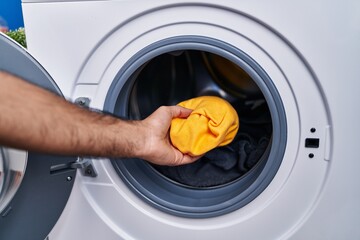 Young hispanic man putting clothes on washing machine at laundry room