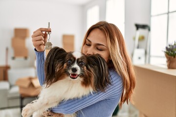Young caucasian woman holding key kissing dog at new home