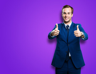 Obraz premium Cheerful smiling businessman in blue confident suit showing two thumbs up like hand gesture, over violet purple color background with copy space for ad, slogan or text. Successful business man.