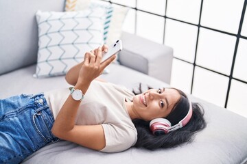 Young beautiful hispanic woman listening to music lying on sofa at home