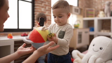 Teacher and preschool student playing with cars toy and ball standing at kindergarten