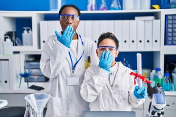 Mother and son at scientist laboratory covering mouth with hand, shocked and afraid for mistake....