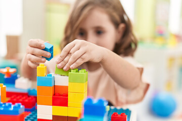 Adorable hispanic girl playing with construction blocks sitting on table at kindergarten