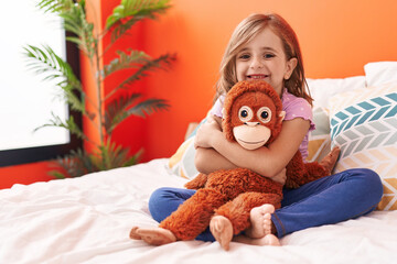 Adorable hispanic girl hugging monkey doll sitting on bed at bedroom