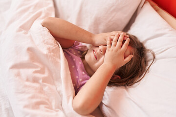 Adorable hispanic girl stressed with hands on eyes lying on bed at bedroom