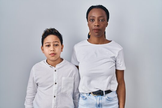 Young Mother And Son Standing Together Over White Background Relaxed With Serious Expression On Face. Simple And Natural Looking At The Camera.