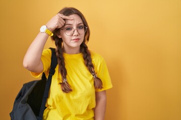 Young caucasian woman wearing student backpack over yellow background pointing unhappy to pimple on...