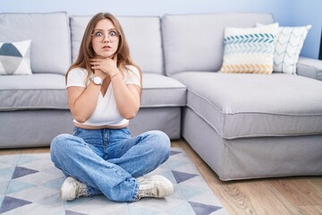 Young caucasian woman sitting on the floor at the living room shouting suffocate because painful strangle. health problem. asphyxiate and suicide concept.