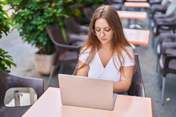 Young blonde woman using laptop sitting on table at coffee terrace