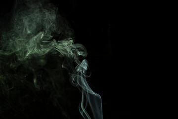 incense stick with green smoke against black background