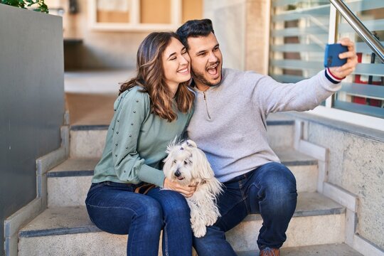Man and woman holding dog making selfie by the smartphone at street