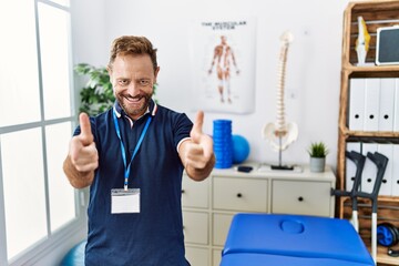 Obraz premium Middle age physiotherapist man working at pain recovery clinic pointing fingers to camera with happy and funny face. good energy and vibes.