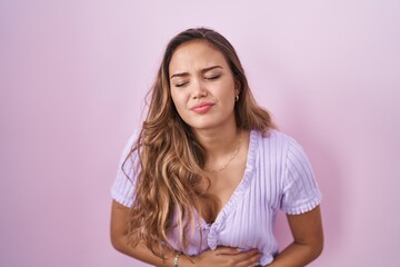 Obraz premium Young hispanic woman standing over pink background with hand on stomach because indigestion, painful illness feeling unwell. ache concept.