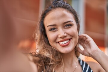 Young beautiful hispanic woman smiling confident making selfie by camera at street
