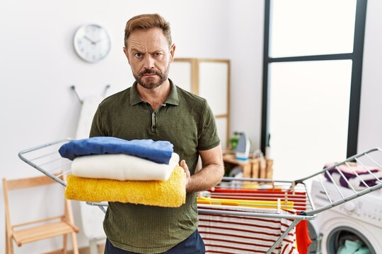 Middle age man holding folded laundry after ironing skeptic and nervous, frowning upset because of problem. negative person.