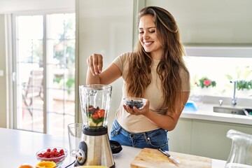 Young beautiful hispanic woman preparing vegetable smoothie with blender at the kitchen