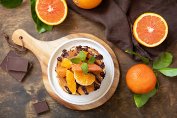Celebrating Pancake day, healthy american breakfast. Delicious bananas pancakes with chocolate and red oranges on rustic table. View from above.