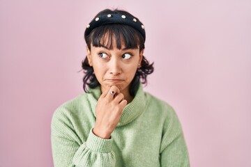 Young beautiful woman standing over pink background thinking worried about a question, concerned and nervous with hand on chin