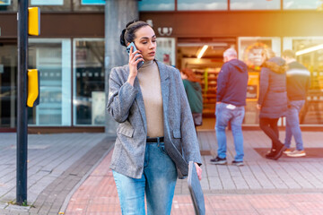 a business woman in a jacket and jeans crossing the road and talking on the phone