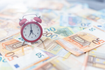 Red alarm clock and euro banknotes of various denominations on a white background.