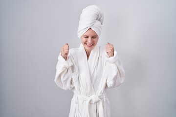 Blonde caucasian woman wearing bathrobe excited for success with arms raised and eyes closed celebrating victory smiling. winner concept.