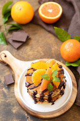 Celebrating Pancake day, healthy american breakfast. Delicious bananas pancakes with chocolate and red oranges on rustic table.