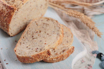 Sliced fresh baked whole grain bread with flax seeds and sesame seeds on light blue board. Bakery products