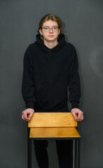 Portrait of a young guy standing next to a chair calmly looking at the camera