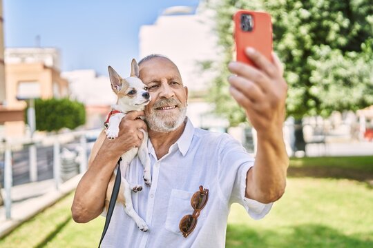 Senior man smihugging chihuahua making selfie by the smartphone at park